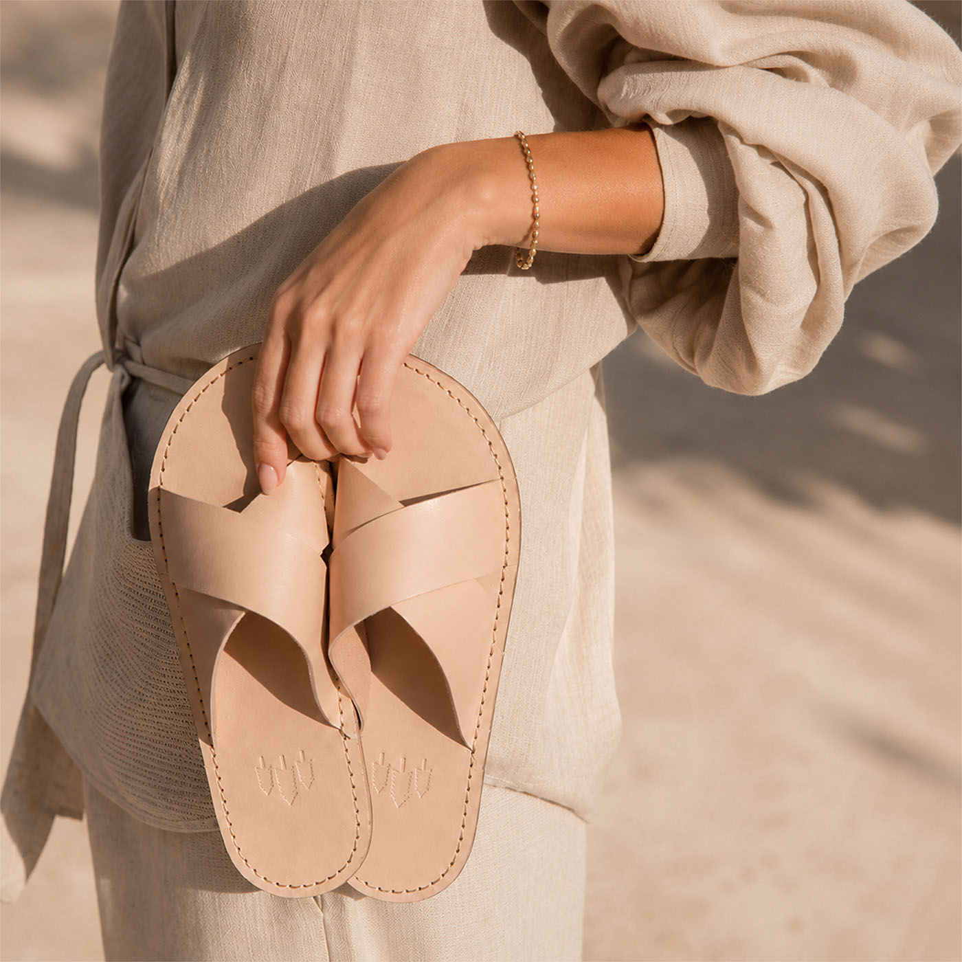 Crema | Close-up of model holding up cream-colored leather flat sandals