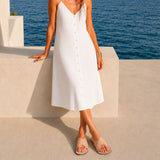 Crema | Close-up of model wearing a white button-down dress and cream-colored leather flat sandals against an ocean background