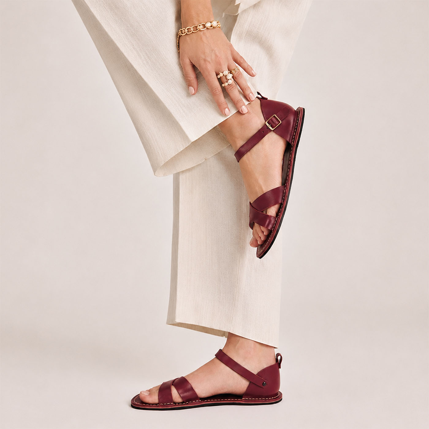 Marsala | Close-up of model wearing flat sandals with an ankle strap and buckle, shown against a plain background