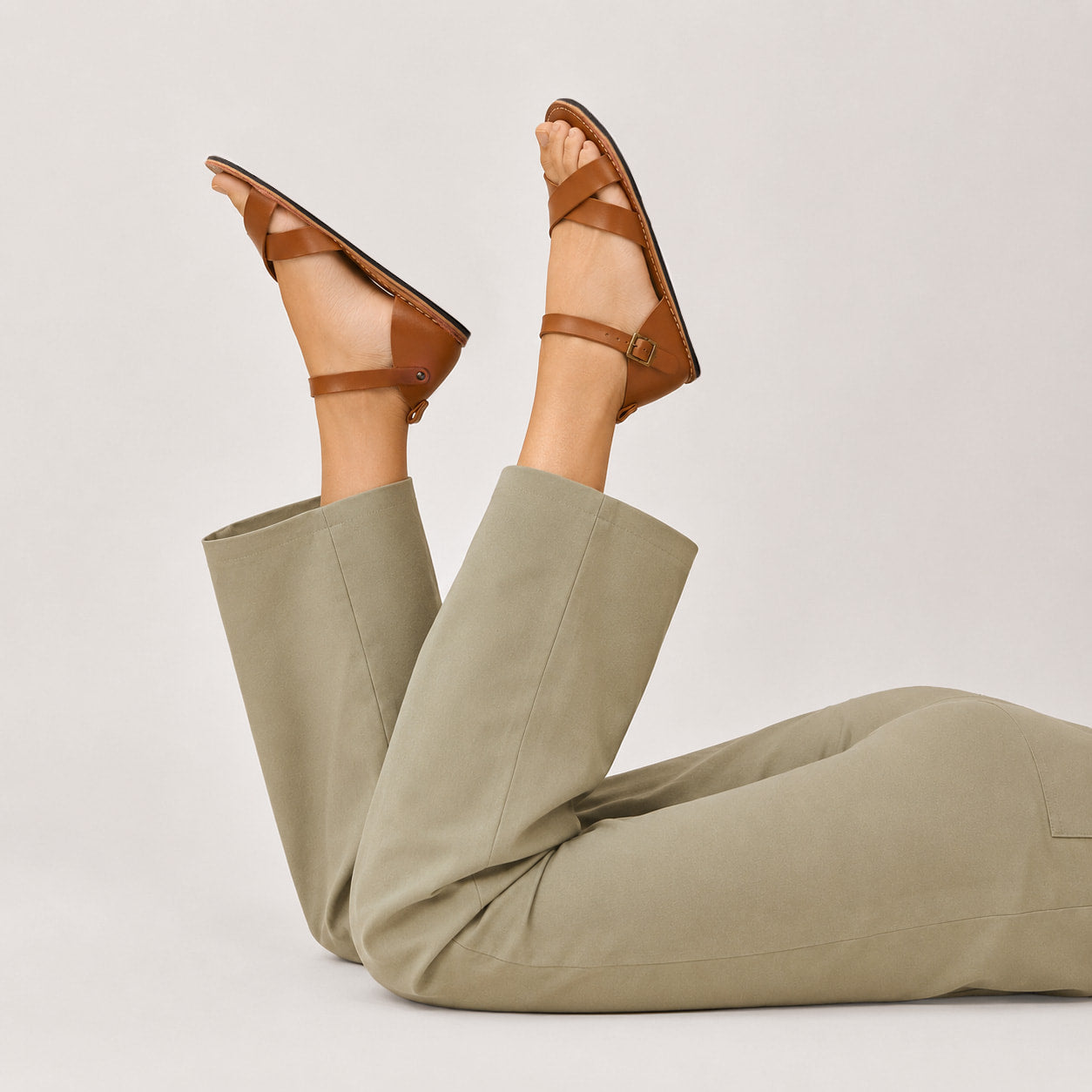 Miele | Close-up of model wearing flat sandals with an ankle strap and buckle, shown against a plain background