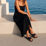 Nero | Model wearing black leather flat sandals against a beachfront background
