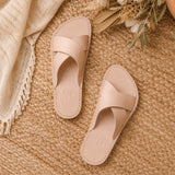 Crema | Cream-colored leather flat sandals with debossed Portland leather tree logo set on a woven mat and bouquet of flowers