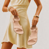 Crema | Close-up of model holding flat sandals with an ankle strap and buckle, shown against a plain background