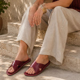 Marsala | Close-up of model wearing gray pants and red wine colored-leather flat sandals sitting on concrete steps