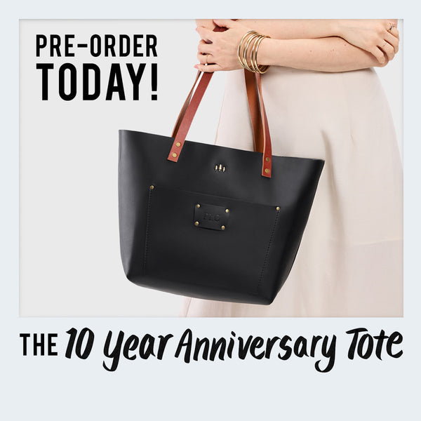 Black tote bag with brown handles held by a person, promotional text for 10-year anniversary tote.