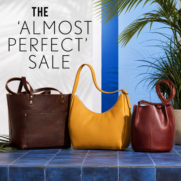 Three leather handbags in Coldbrew, Sunshine, and Nutmeg on a blue tiled surface with palm leaves in the background. Text: The 'Almost Perfect' Sale