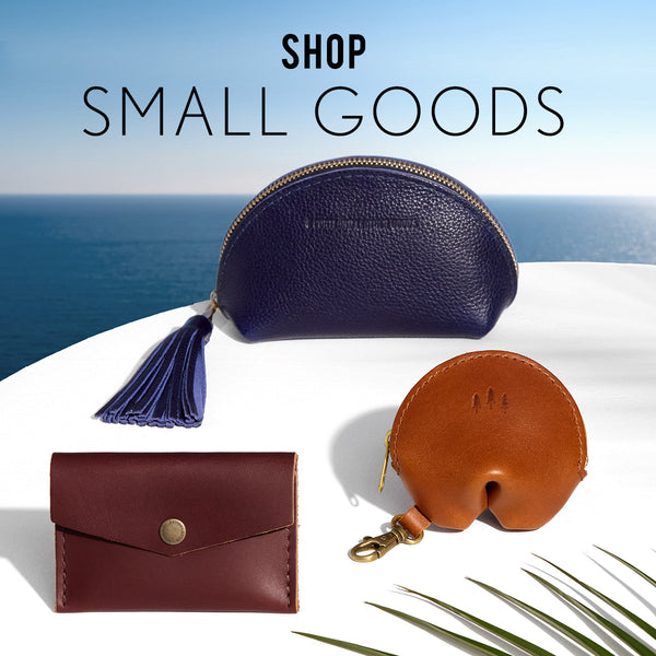 Three leather pouches in blue, brown, and red on a white surface with a blue sky background. Text: Shop Small Goods.
