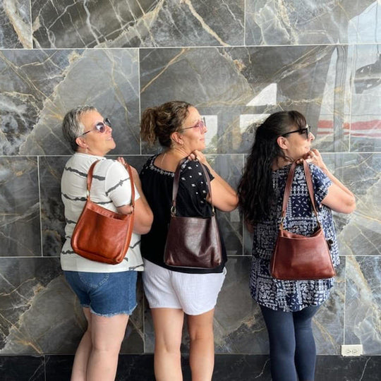 Three women standing against a tiled wall, each holding a Triangle Shoulder Bag.