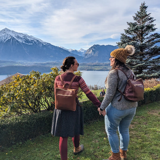 Two people holding hands with Tote Backpacks, standing in a scenic area with mountains and trees.