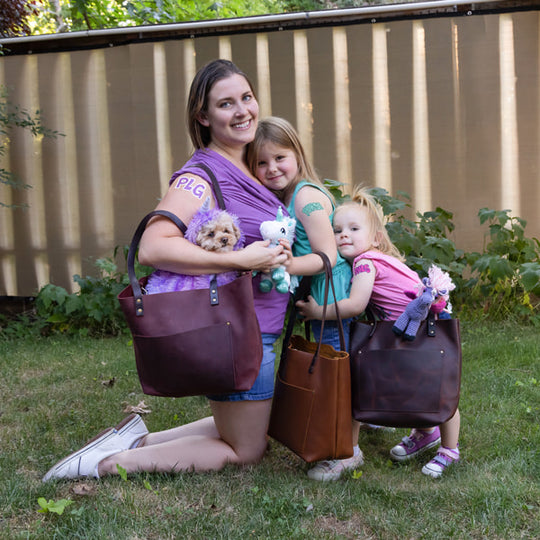 Woman and two children outdoors with plush toys, posing in front of a wooden fence using three Leather Tote Bags.