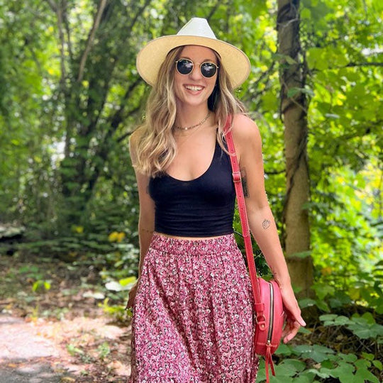 A person posed on a paved trail in a wooded area with a Ruby Circle Crossbody on one shoulder