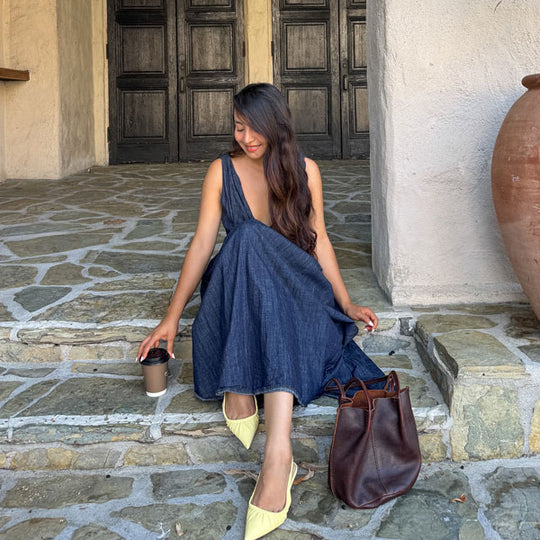Person sitting on stone steps reaching for a coffee next to a Classic Devan Bucket Tote in Coldbrew