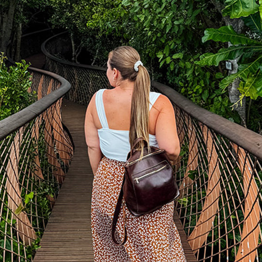 Model outside on a wooden bridge wearing a brown tote backpack
