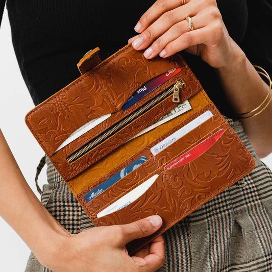 Model holding leather bifold wallet with snap closure open in meadow