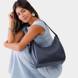 Night Owl Medium | Model holding u-shaped, flat-bottomed leather shoulder bag with adjustable strap