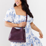 Plum | Model wearing a symmetrical bucket bag with latch closure and removable crossbody strap
