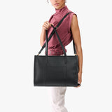 Black Oversized East/West | Model holding structured wide tote bag with overlapping panels and crossbody strap