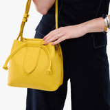 Canary Small | Model holding symmetrical leather bag with leather drawstring closure and adjustable shoulder strap