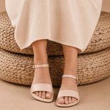 Crema | Close-up of a person wearing light green cropped pants and cream flat sandals with an ankle strap and buckle, shown against a plain background.