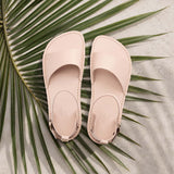 Crema | Close-up of a person wearing light green cropped pants and cream flat sandals with an ankle strap and buckle, shown against a plain background.