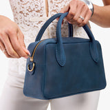 Deep Water Large | A large bowler styled bag with a crossbody strap being held by a model in a white outfit