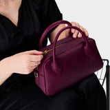 Lollipop Large | A large bowler styled bag with a crossbody strap being held by a model wearing a black dress