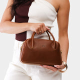 Nutmeg Large | A bowler styled bag with a crossbody strap being held by a model wearing a brown and white top