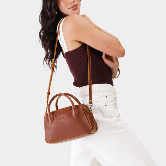 Nutmeg*Large | A bowler styled bag with a crossbody strap being worn by a model wearing a brown and white top