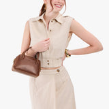 Asheville Small | A bowler styled bag with a crossbody strap being held by a model wearing a dress