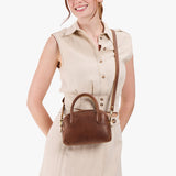 Asheville Small | A bowler styled bag with a crossbody strap being held by a model wearing a dress