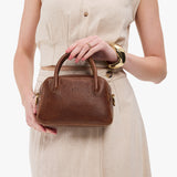 Asheville Small | A bowler styled bag with a crossbody strap being held by a model wearing a dress