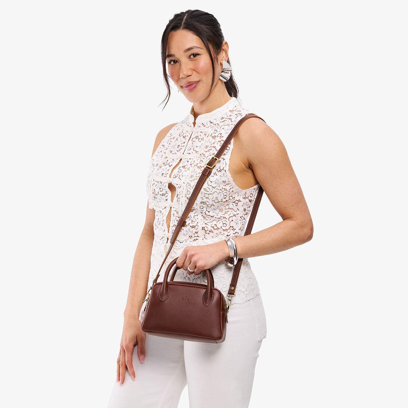 Cognac*Small | A bowler styled bag with a crossbody strap being worn by a model in a white outfit