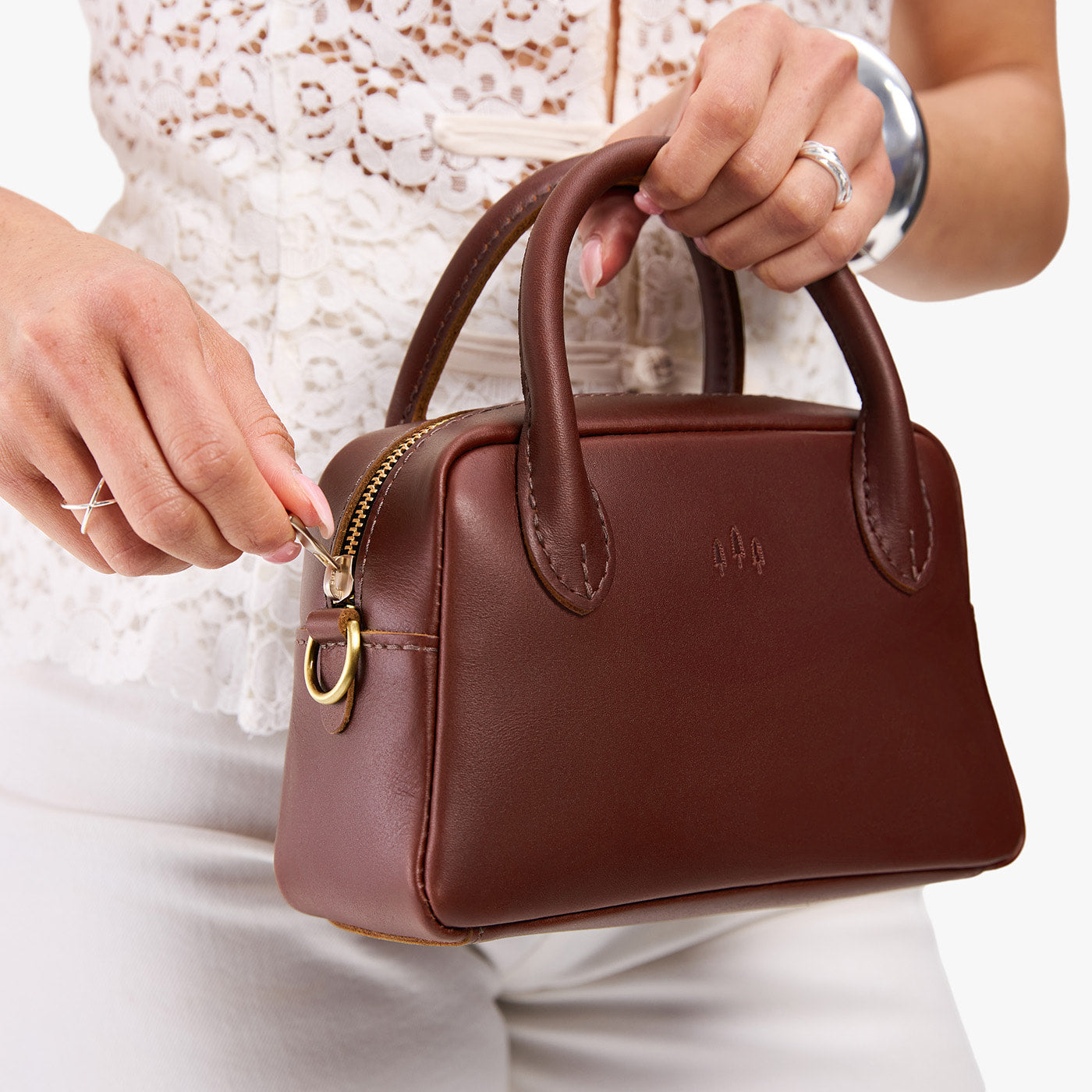 Cognac*Small | A bowler styled bag being held by a model in a white outfit