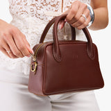 Cognac Small | A bowler styled bag being held by a model in a white outfit