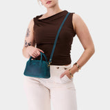  Westward Blue Small | Bowler styled bag with a crossbody strap being worn by a model in a brown shirt 
