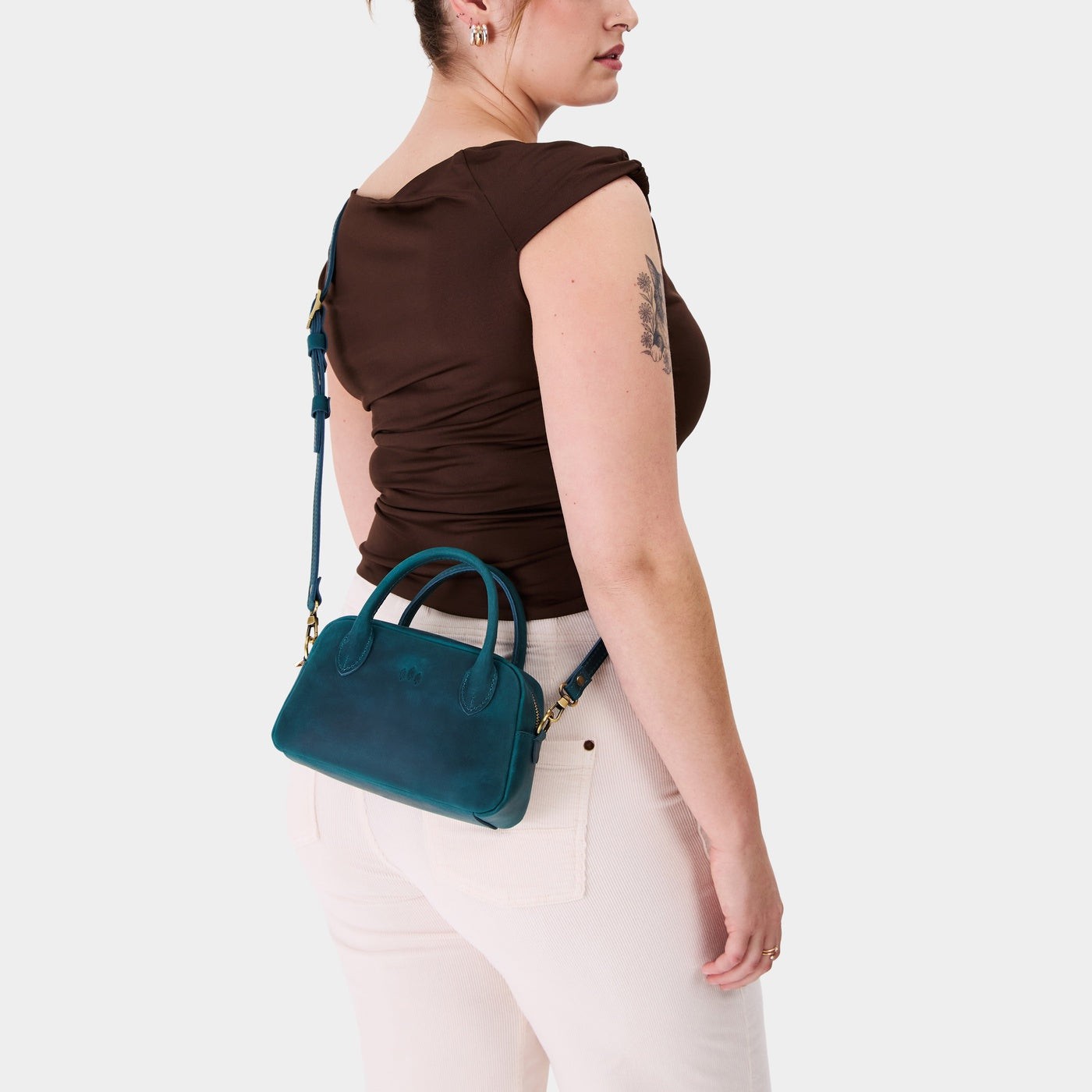 Westward Blue*Small | A bowler styled bag with a crossbody strap being worn by a model in a brown shirt 