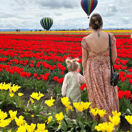 Adult and child in a tulip field with hot air balloons in the background, wearing a Small Black Circle Crossbody.