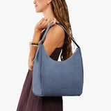 Denim Large | Model holding u-shaped, flat-bottomed leather shoulder bag with adjustable strap