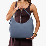 Denim Large | Model holding u-shaped, flat-bottomed leather shoulder bag with adjustable strap