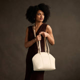 Pebbled Bone Large | Model holding a half circle crossbody bag with handles and removable crossbody strap