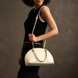 Pebbled Bone Small | Model holding a half circle crossbody bag with handles and removable crossbody strap