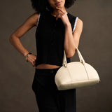 Pebbled Bone Small | Model holding a half circle crossbody bag with handles and removable crossbody strap