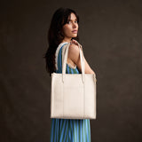 Pebbled Bone North/South | Model holding structured large tote bag with overlapping panels and crossbody 