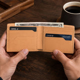 Naturale | A leather bifold wallet held open by two hands over a dark wooden table, with cash and cards visible inside. 