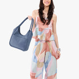 Denim Large | A model holding a u-shaped, flat-bottomed leather shoulder bag with two outside pockets