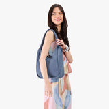 Denim Large | A model holding a u-shaped, flat-bottomed leather shoulder bag with two outside pockets