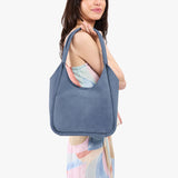 Denim Large | A model holding a u-shaped, flat-bottomed leather shoulder bag with two outside pockets