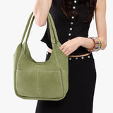Laurel Large | A model holding a u-shaped, flat-bottomed leather shoulder bag with two outside pockets
