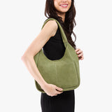 Laurel Large | A model holding a u-shaped, flat-bottomed leather shoulder bag with two outside pockets