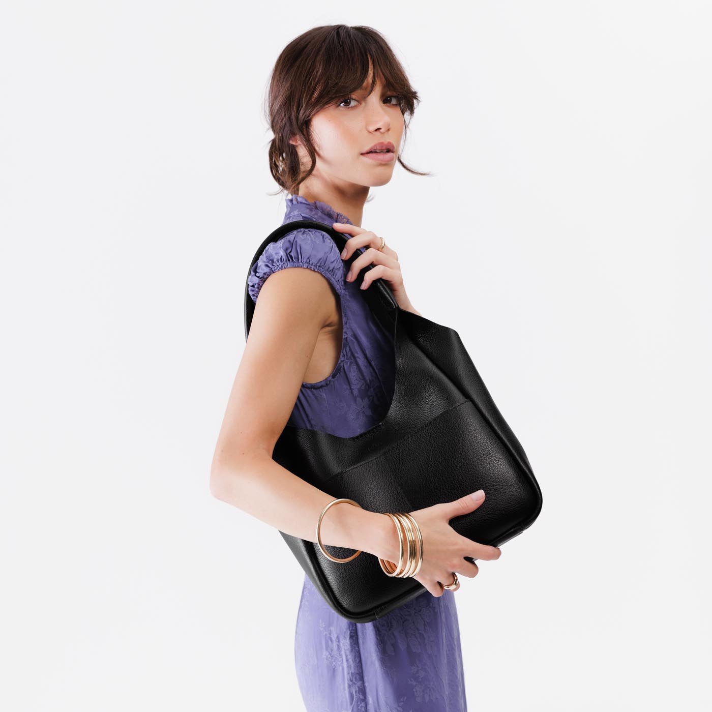 Pebbled--Black*Large | A model holding a u-shaped, flat-bottomed leather shoulder bag with two outside pockets